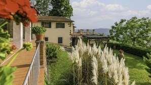 Una villa con terraza de madera, jardín con hierbas altas y vistas a las montañas.