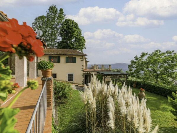 Una villa con terraza de madera, jardín con hierbas altas y vistas a las montañas.