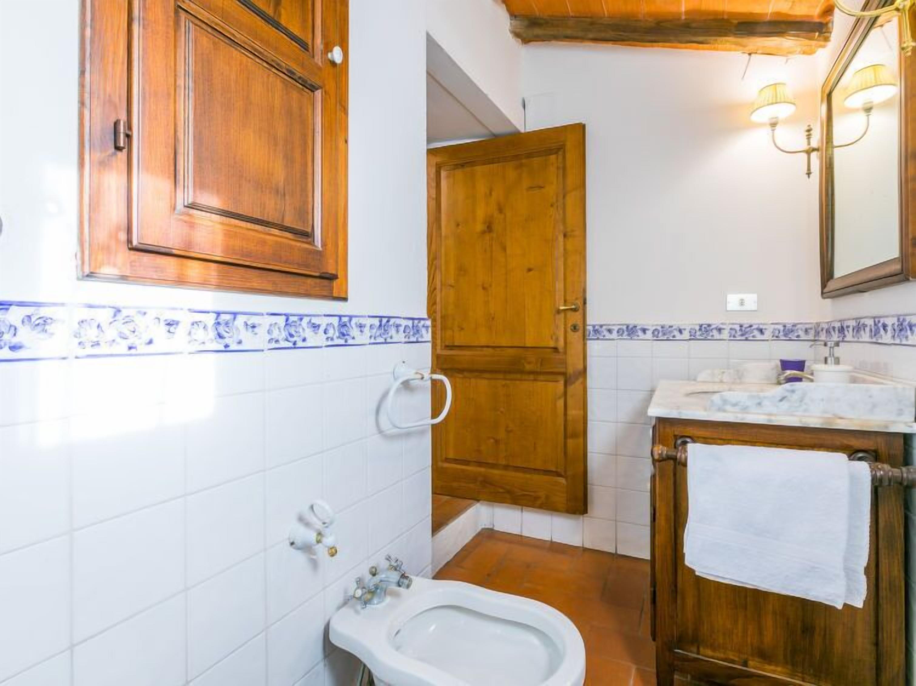 Un baño con bidé, un mueble de madera y un espejo con luces empotradas.