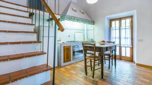 Una cocina con una mesa de comedor y sillas, una escalera con escalones de madera, y un ventanal con cortinas.