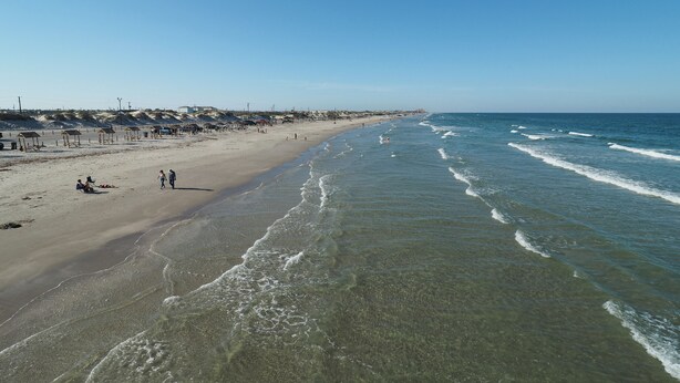 Una playa con aguas cristalinas, orilla de arena y cabañas de playa.
