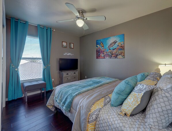 A bedroom with a bed, a TV, a ceiling fan, and a window with curtains.