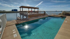 Una piscina azul cristalina con una terraza de madera y un área de estar cubierta.