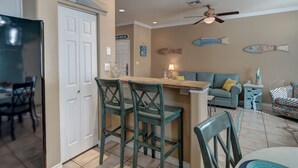 Una cocina con comedor, ventilador de techo y decoración en la pared con motivos marinos.