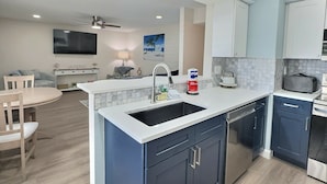 A modern kitchen with a central island, built-in cabinets, and a dining area with a table and chairs. - Siesta Beach Condo Rental with direct beach and pool access (Siesta Key)