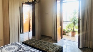 A bedroom with a bed, a chandelier, a sliding glass door leading to a balcony, and a potted plant outside. - Residenza Donna Maria (Ercolano)