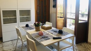 A dining area with a table set for two, chairs, a buffet cabinet, and a door leading to an outdoor balcony. - Residenza Donna Maria (Ercolano)