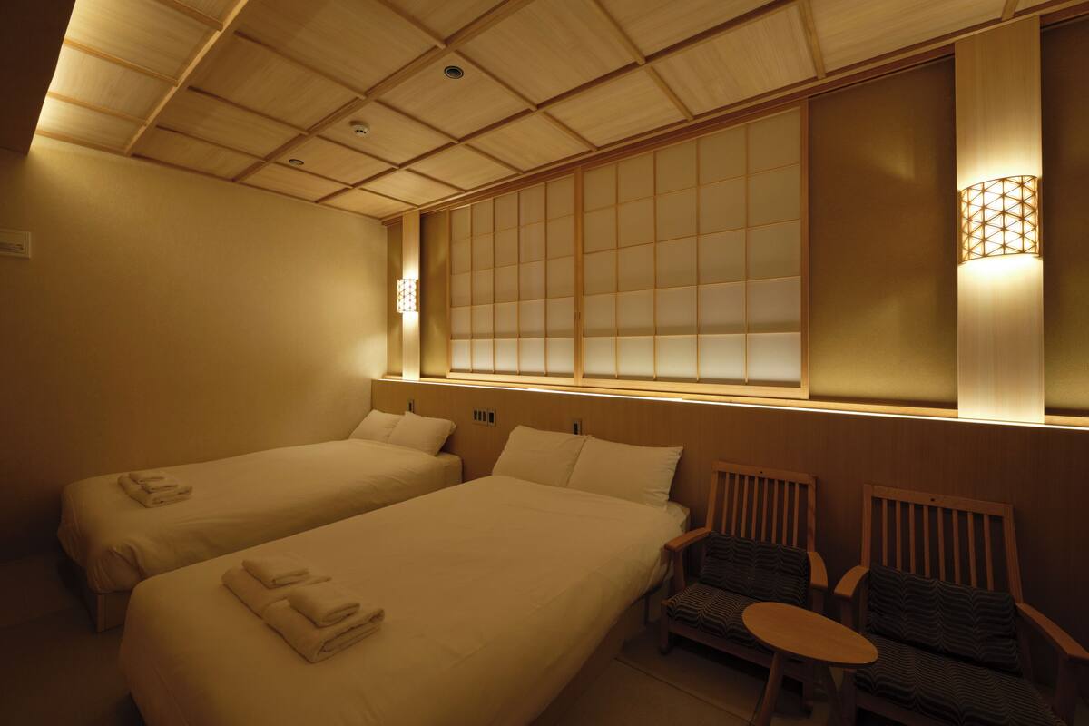 A hotel room with two beds, a small table, and a chair.