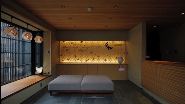 Un vestíbulo de hotel con una recepción, una zona de estar con un banco acolchado, una pared decorativa con una luna y estrellas, y un techo de madera con iluminación empotrada.