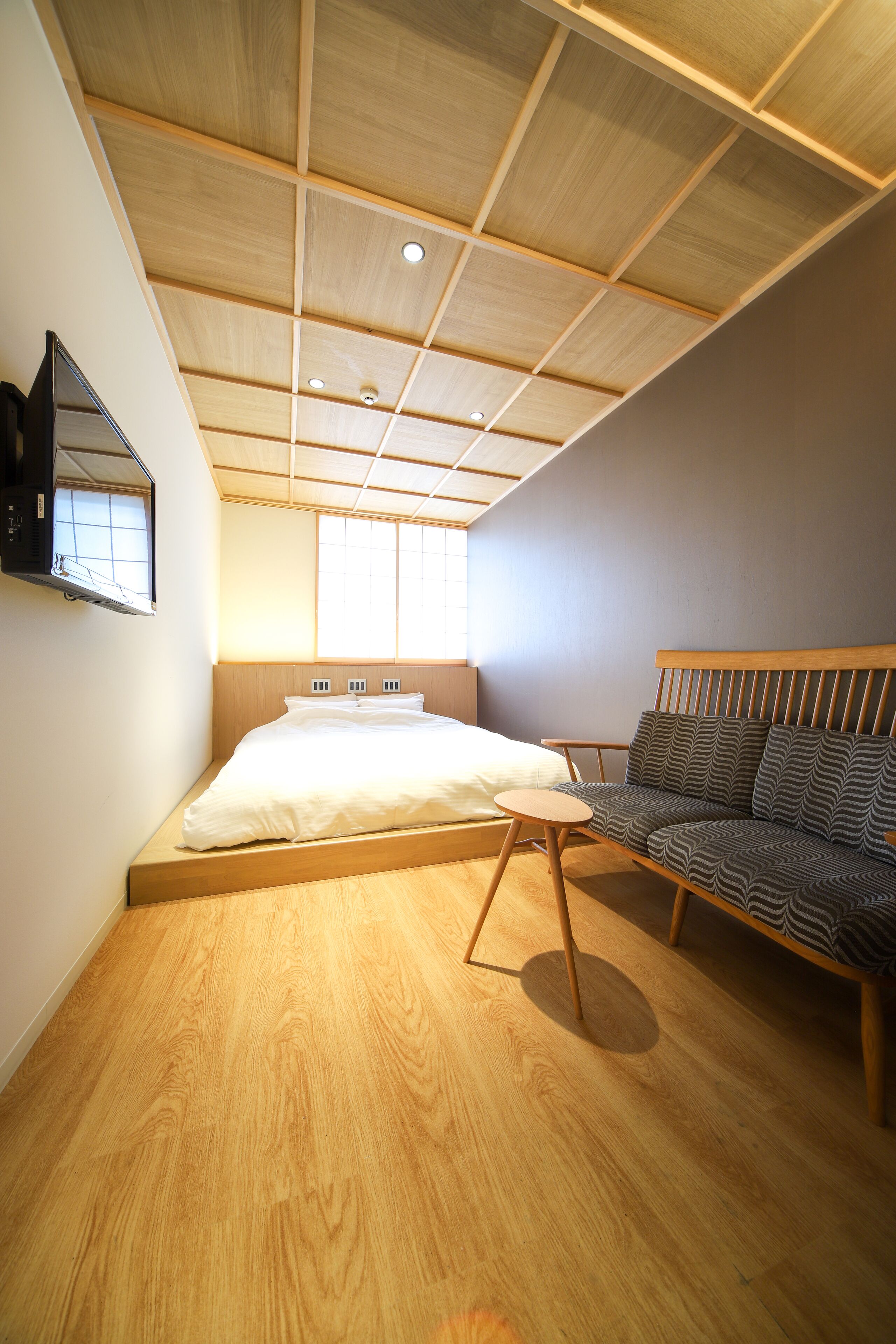 A bedroom with a wooden ceiling, a bed, a sofa, and a small table.