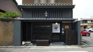 Un edificio japonés tradicional de fachada oscura, entrada con listones de madera y un cartel que indica que es un hotel.