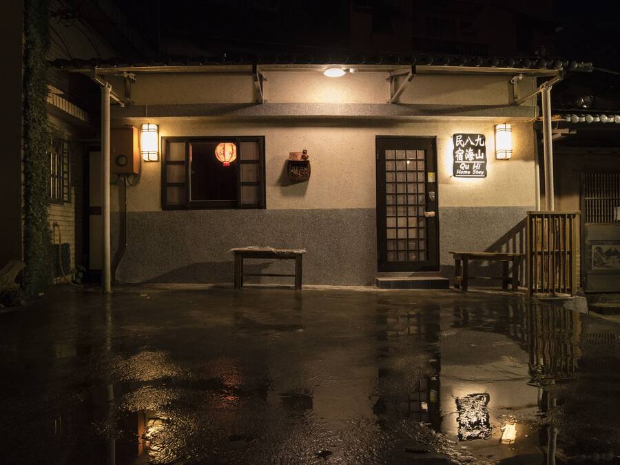 A traditional Japanese-style building with a wooden bench in front, a small table, and a lantern on the wall.