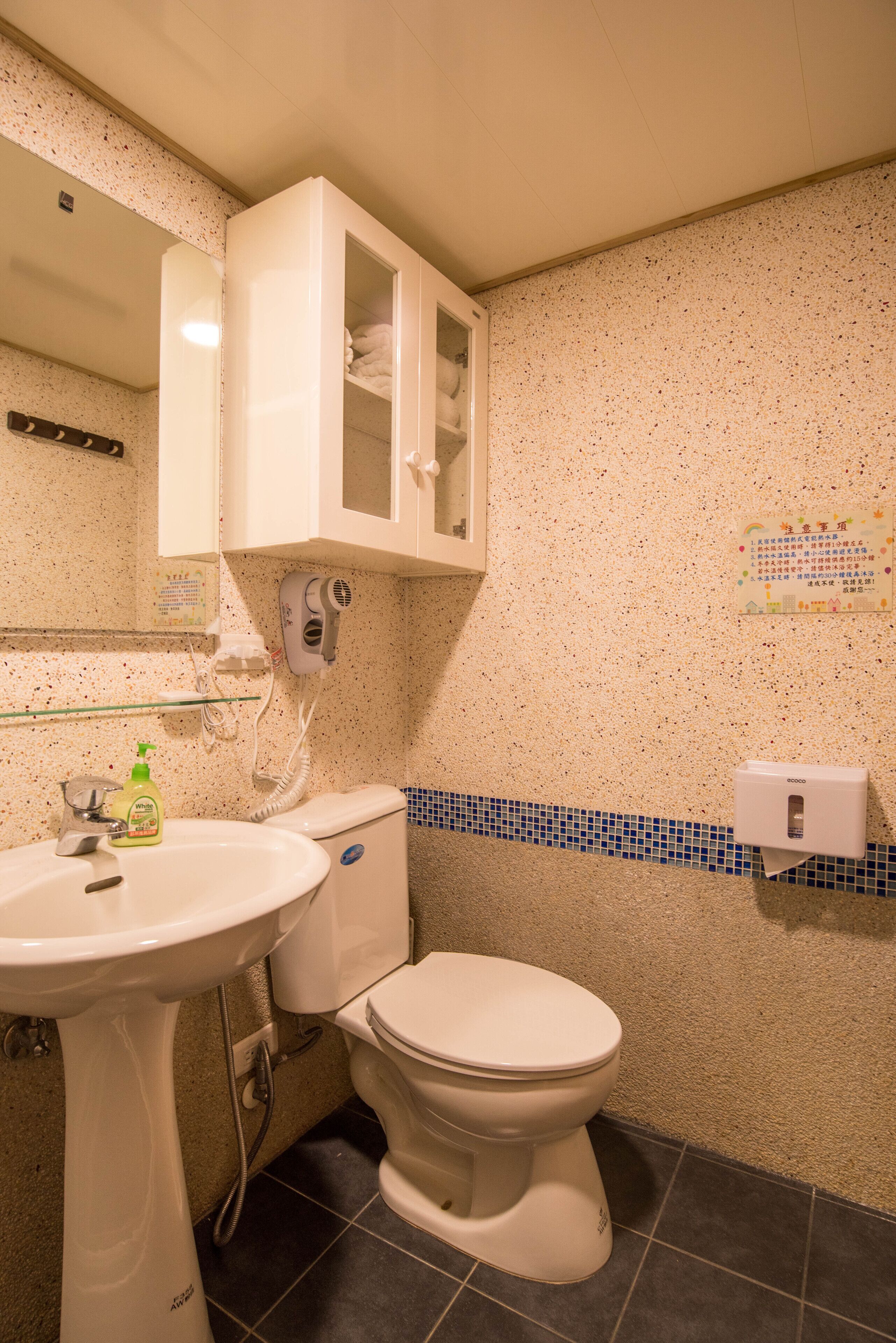 A bathroom with a white sink, toilet, and cabinet, a hairdryer, and a soap dispenser.