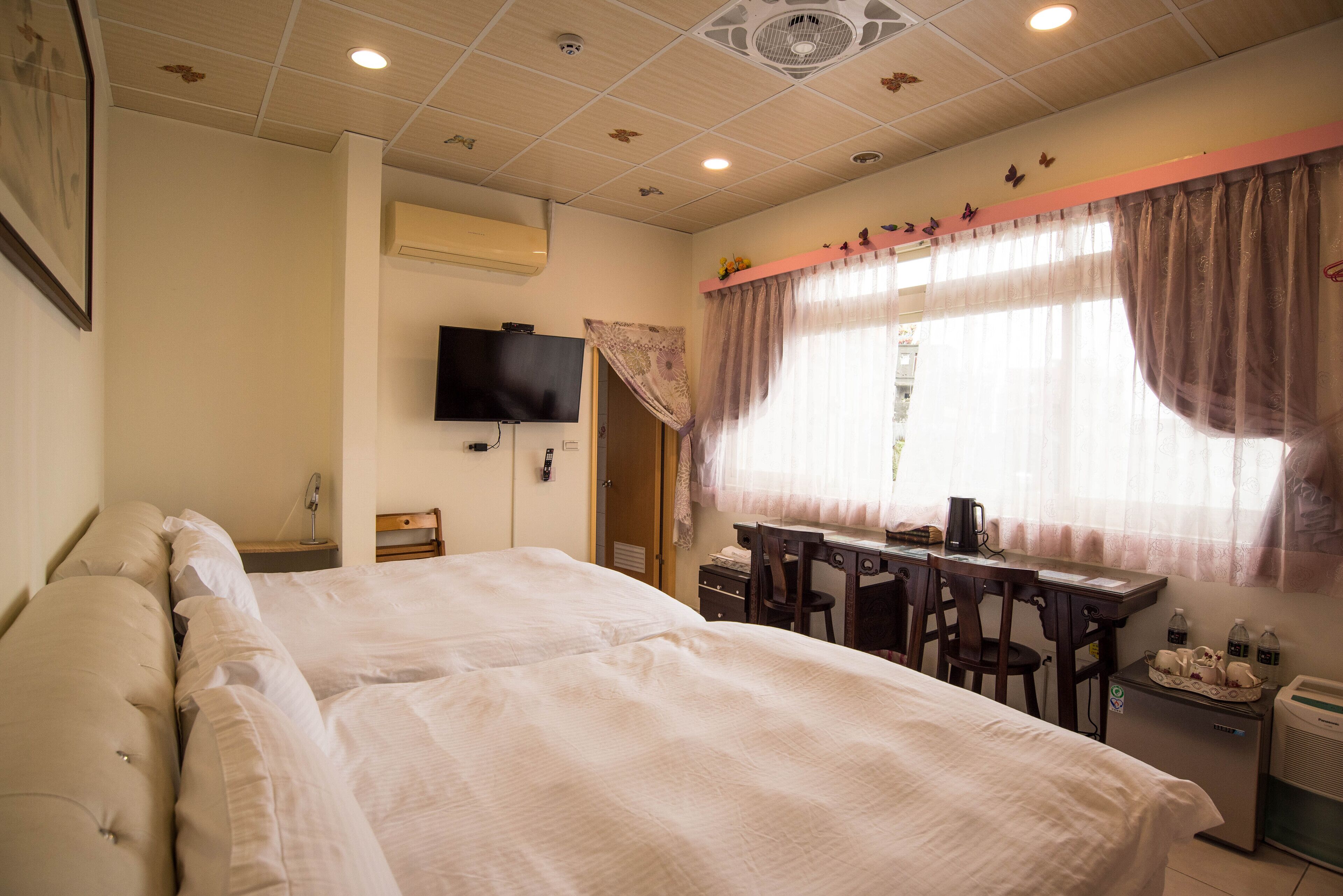 A hotel room with two beds, a desk, a chair, a television, and a window with curtains.