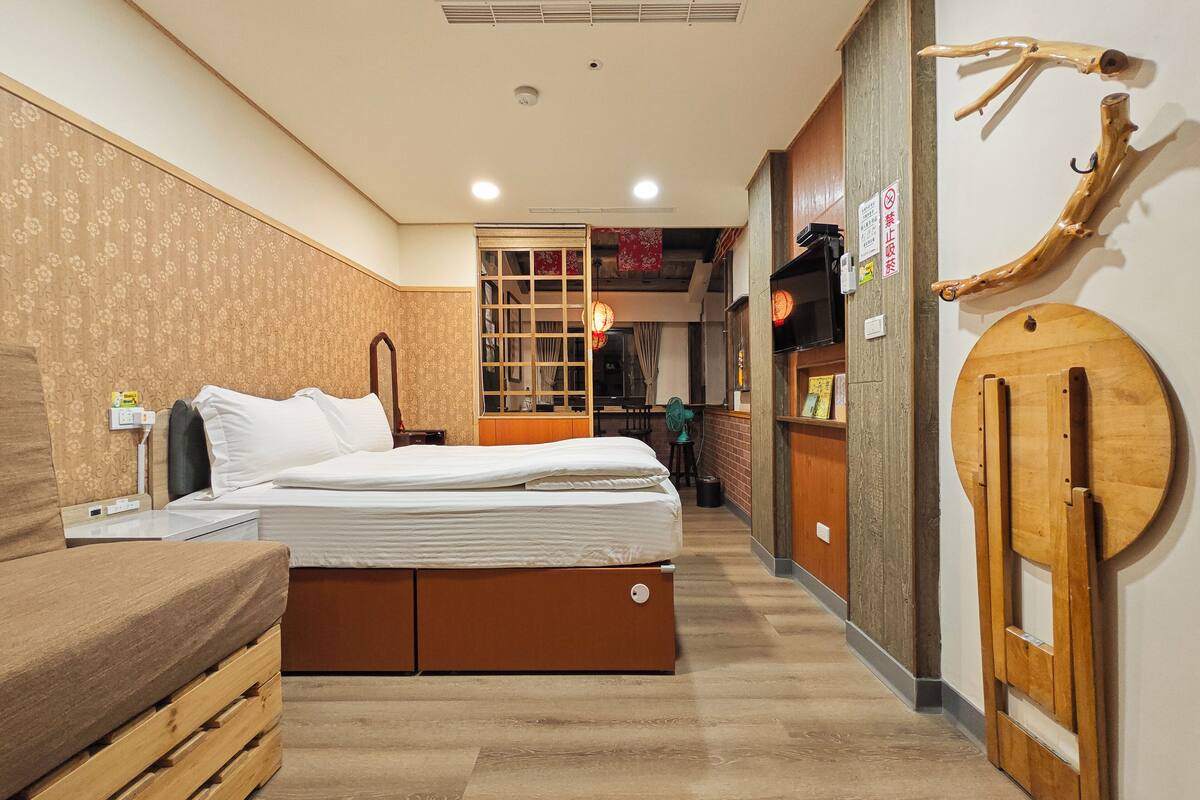 A hotel room with a bed, wooden side table, and a wardrobe.