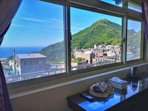 A hotel room with a large window offering a view of a mountainous landscape and a cityscape. - Qu Hi Home Stay (New Taipei City)