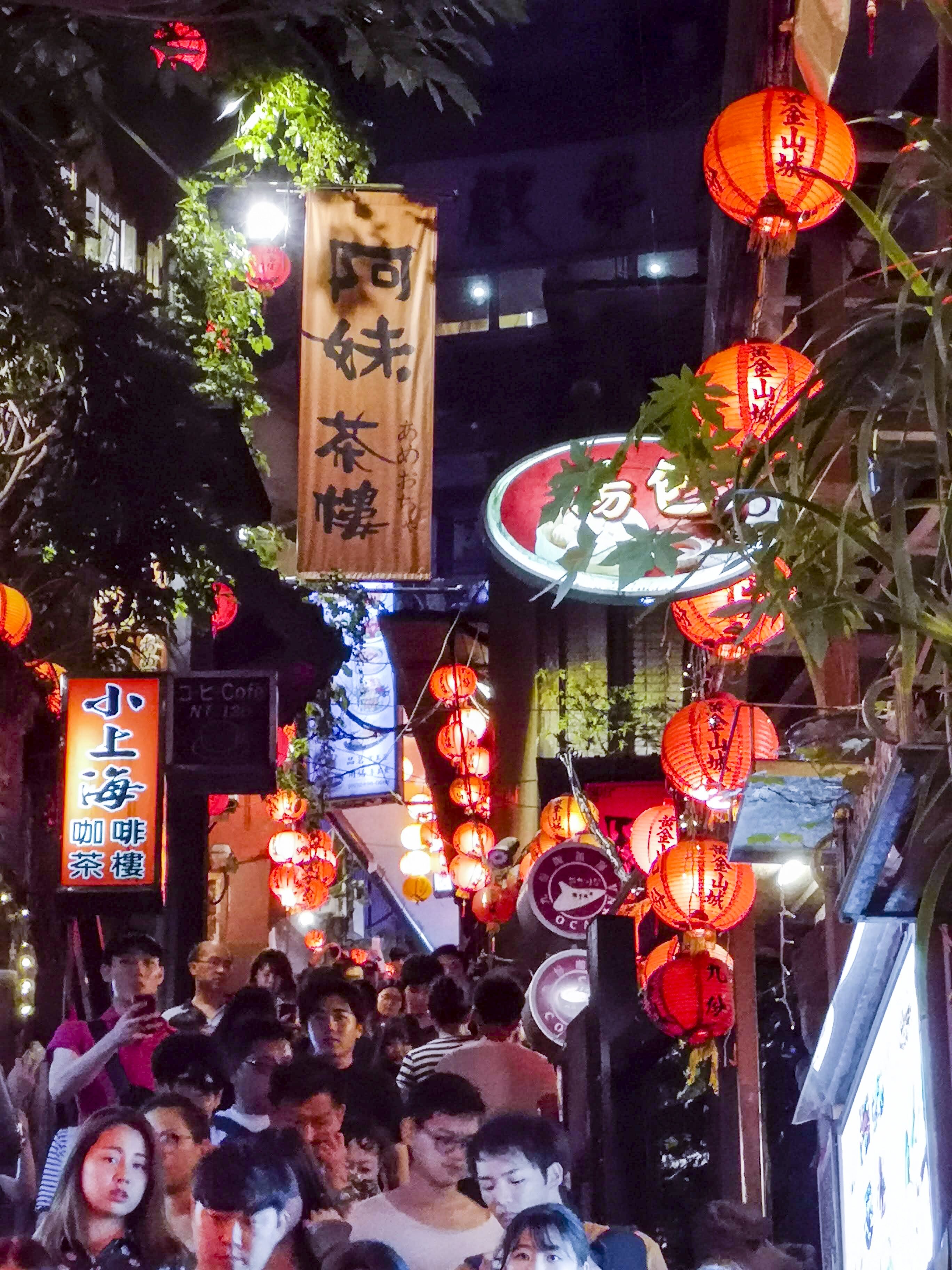 A crowded street at night with traditional red lanterns and signs in a foreign language.
