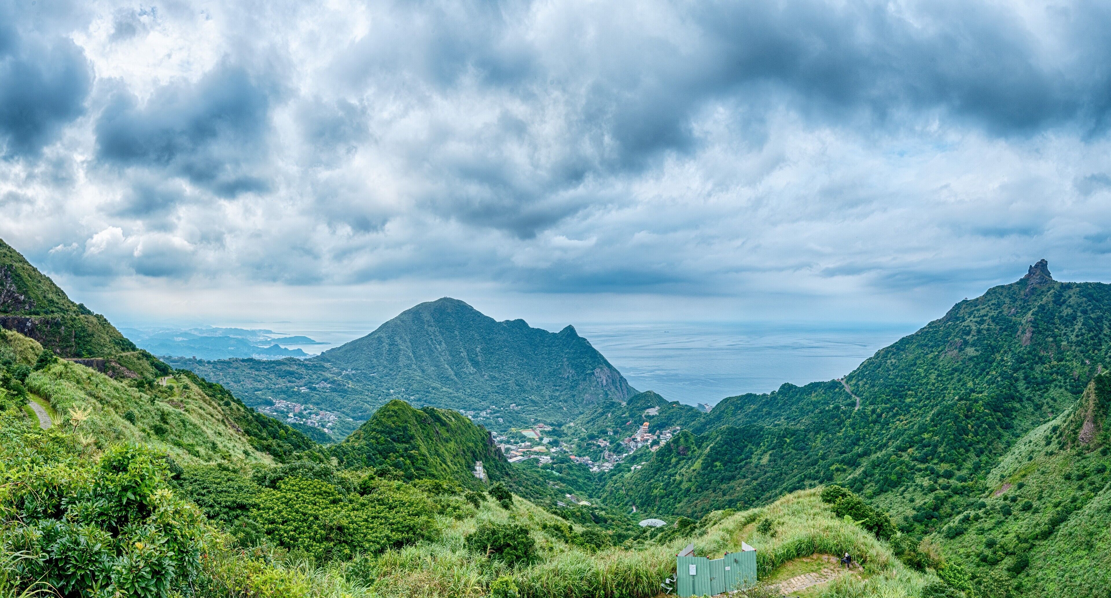 A mountainous landscape with lush greenery and a small structure in the foreground.