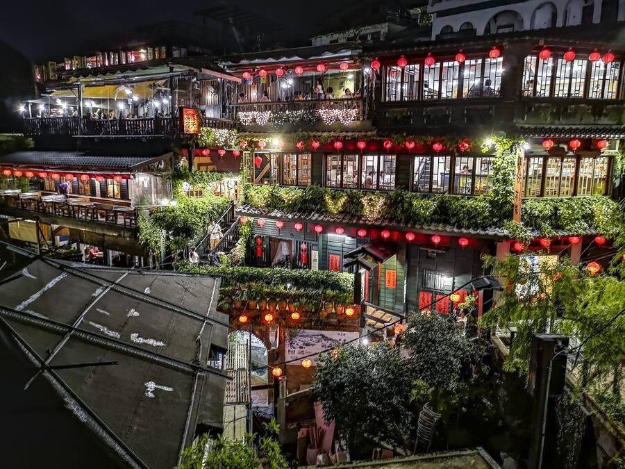 A traditional multi-story building with balconies, red lanterns, and greenery.