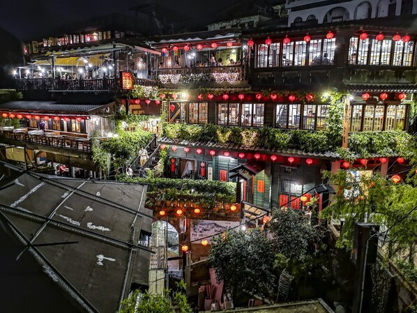 Um edifício tradicional de vários andares, com varandas, lanternas vermelhas e vegetação.