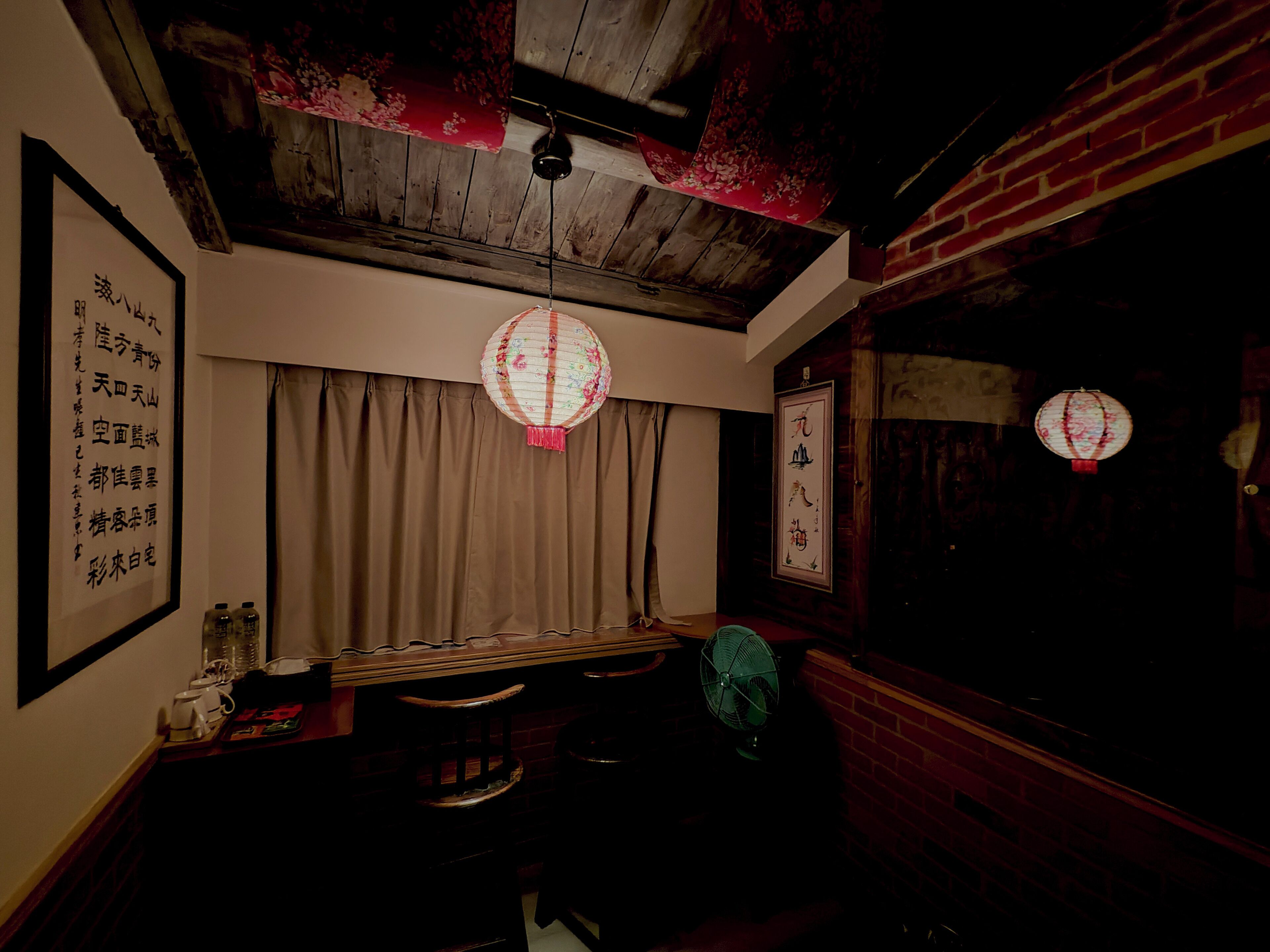 A dimly lit room with a wooden ceiling, a traditional Chinese lantern, and a wall with calligraphy.