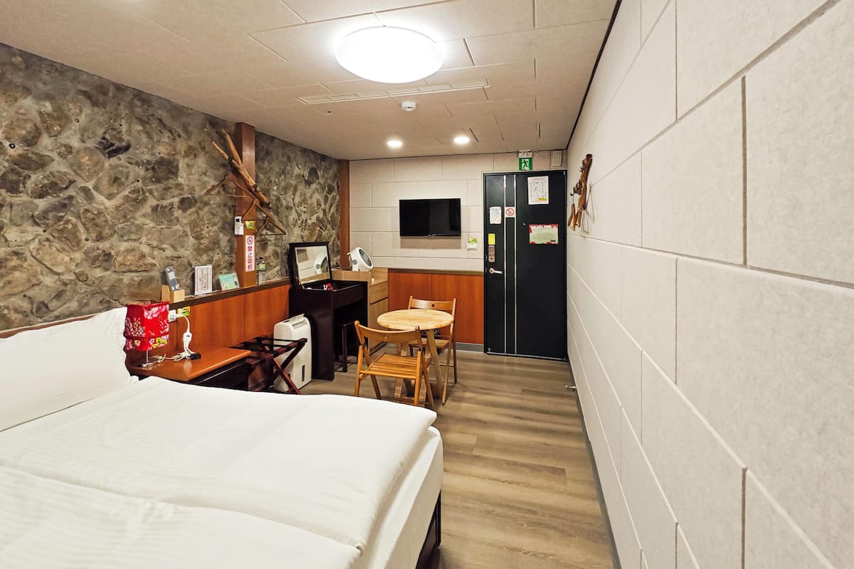 A hotel room with a bed, a desk with a chair, a small round table with chairs, a television, and a wardrobe.