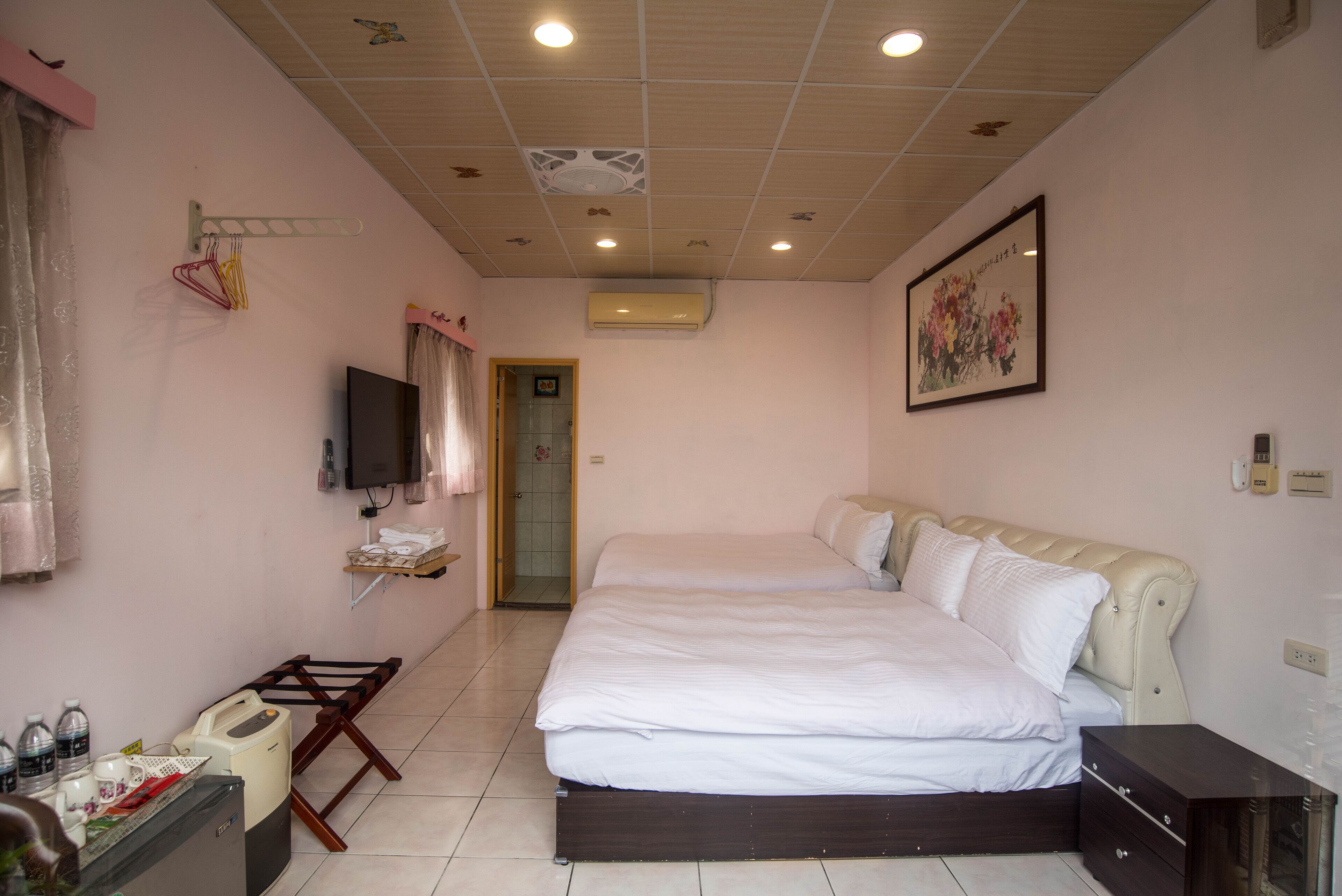A bedroom with a large bed, a TV mounted on the wall, an air conditioning unit, and a door leading to another room.