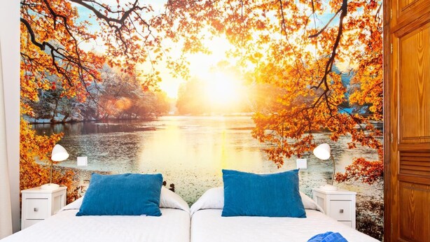 A bedroom with a mural of autumn leaves and a lake, two beds with blue pillows, white bedding, and a blue towel on the bed. - Apartment Tropical Center Playa Blanca By PVL (playa blanca)