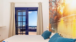 A hotel room with a bed, a view of the sea through a glass door, and a painting of a sunset landscape. - Apartment Tropical Center Playa Blanca By PVL (playa blanca)