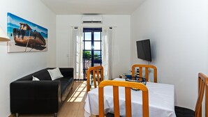 Ein gemütlicher Wohnraum mit einer Couch, Esstisch, Stühlen, einem Fernseher und einem Gemälde eines Bootes an der Wand.