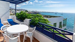 Ein Balkon mit einem weißen Tisch und Stühlen mit Blick auf eine Küstenstadt und das Meer.