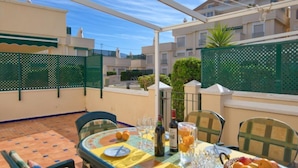 Terraza en la azotea con una mesa para dos, con cubierta de vidrio, sillas y un frutero.