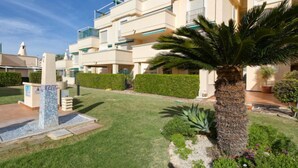 Un moderno edificio residencial de varios pisos, con balcones, un césped cuidado y una palmera.