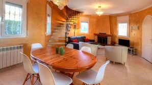 Una sala de estar acogedora con una mesa de comedor de madera, sillas blancas, una chimenea y una escalera que sube a un nivel superior.