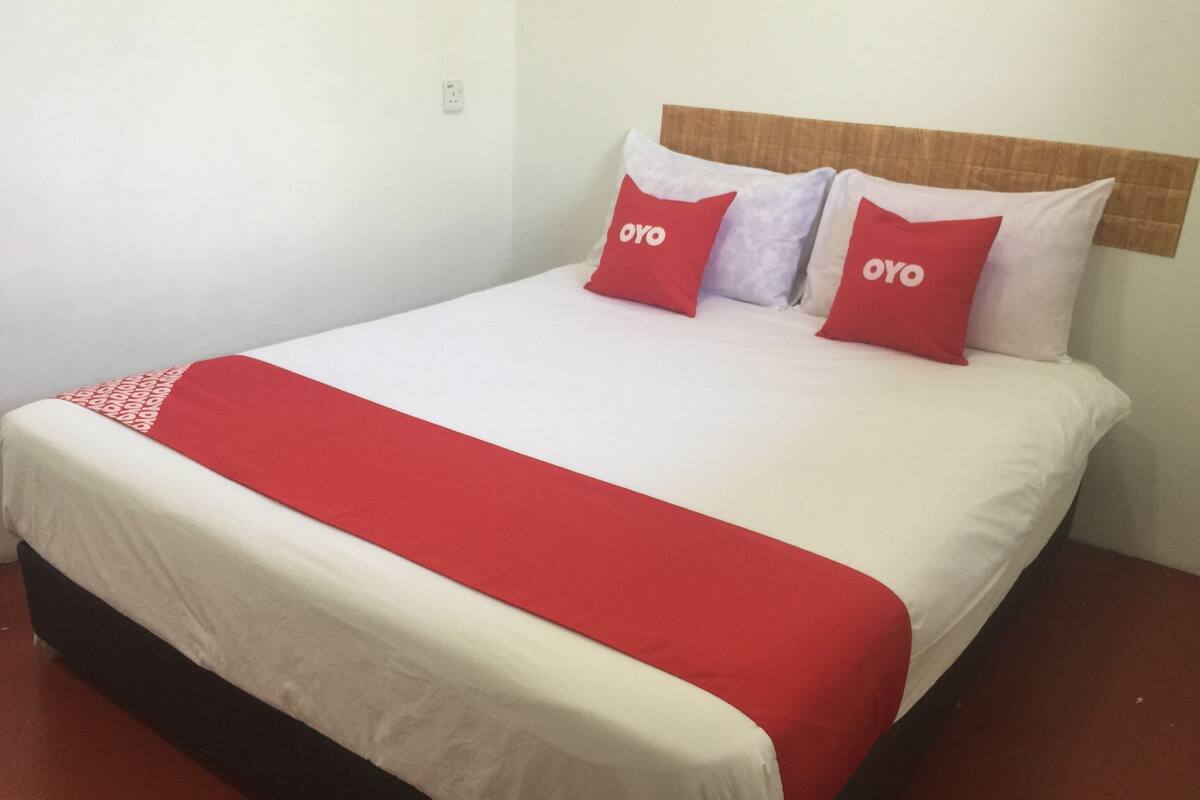 Een bed met een wit en rode spreideken, twee rode kussens met de tekst "OYO" erop, en een houten hoofdbord.
