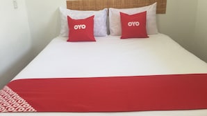 Een bed met twee kussens met daarop het label "OYO" en een rode deken.