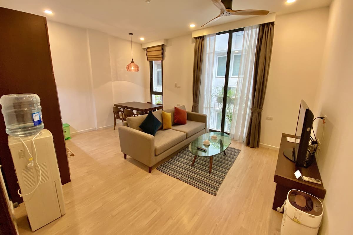 A living room with a sofa, coffee table, and a ceiling fan. There is a water dispenser and a TV on a stand.