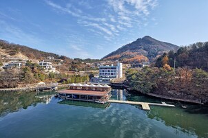 Un hotel a orillas del río con un muelle, una montaña al fondo y cielo despejado.