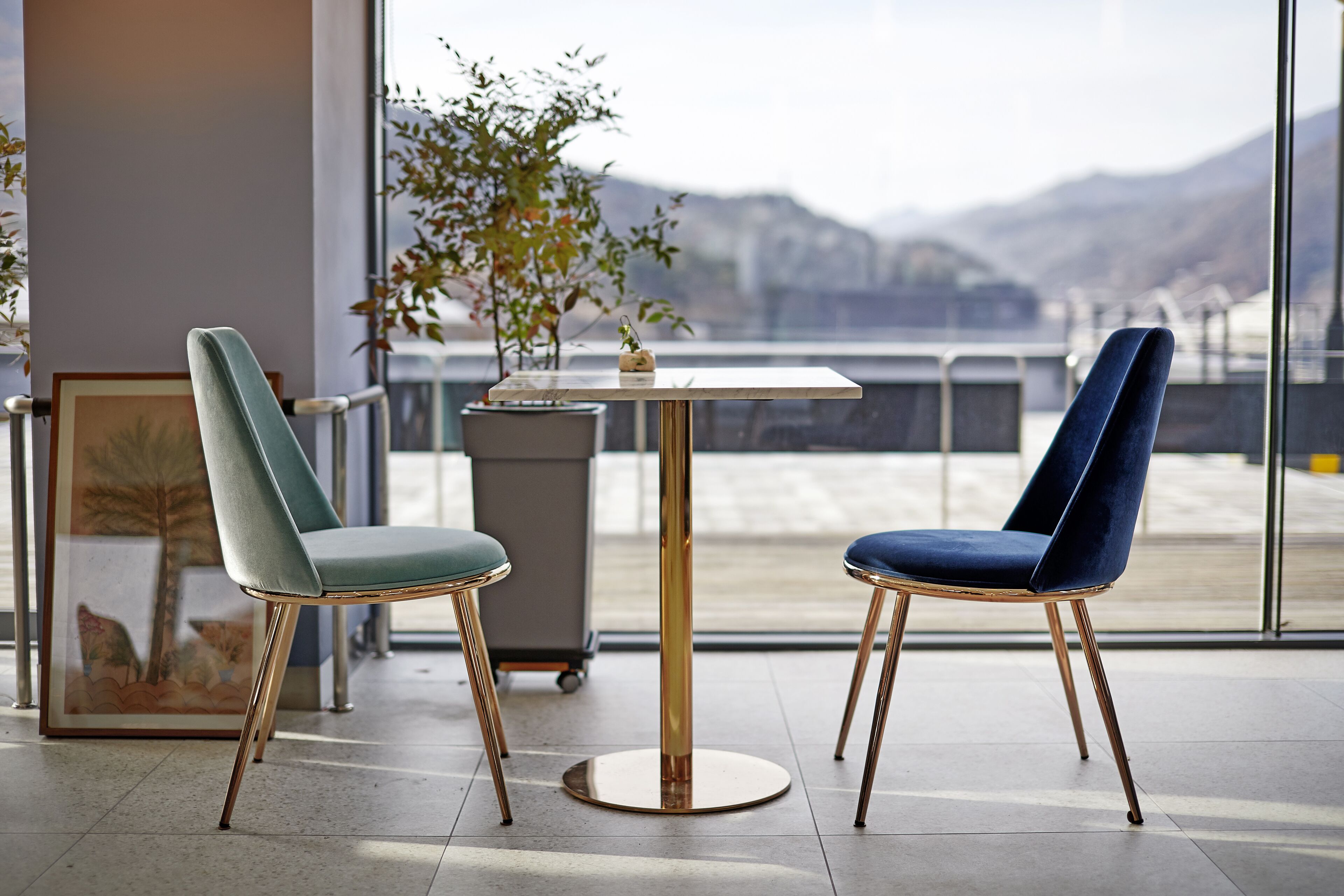 A modern interior with two chairs and a table, a framed picture, and a potted plant.