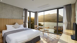 Ein modernes Hotelzimmer mit einem großen Bett, einem Holzkopfteil und Blick auf einen See und Berge.