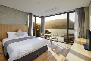 A modern hotel room with a large bed, wooden headboard, and a view of a lake and mountains.