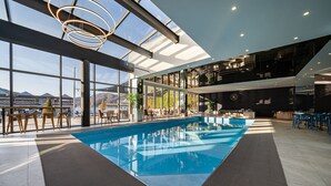 Ein moderner, überdachter Pool mit Glaswänden, Sitzbereichen und Blick auf die Berge.