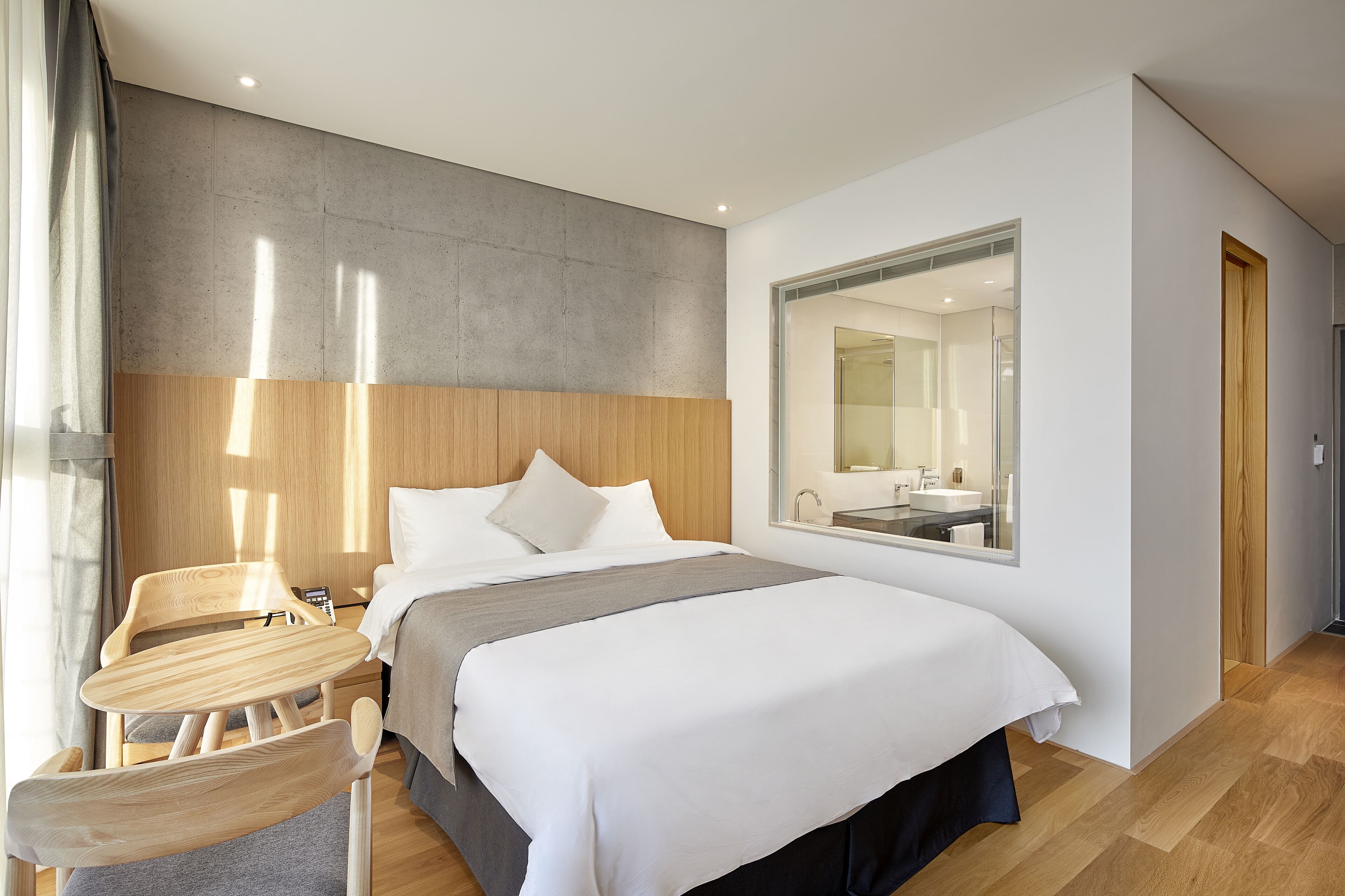 A modern hotel room with a large bed, a wooden desk, a chair, and a mirror.