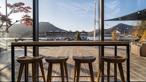 Eine Holzterrasse mit drei Hockern, mit Blick auf eine malerische Berglandschaft und ein Gewässer.