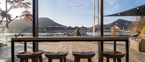 A wooden deck with three stools, overlooking a scenic view of mountains and a body of water.