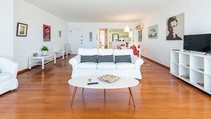 A modern living room with a white sofa, a coffee table, and a TV on a white stand. - Adelos Coastal Chic by the Sea - Athens Riviera (Alimos)