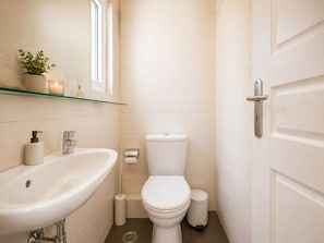 A modern bathroom with a white sink, toilet, and glass shelf with toiletries.