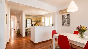 A modern kitchen with white cabinets, a central island, and a dining area with red chairs and a white table. - Adelos Coastal Chic by the Sea - Athens Riviera (Alimos)