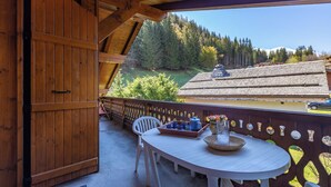 En træterrasse med bord og stole, et dekorativt gelænder og udsigt til et bjerg og en skov.