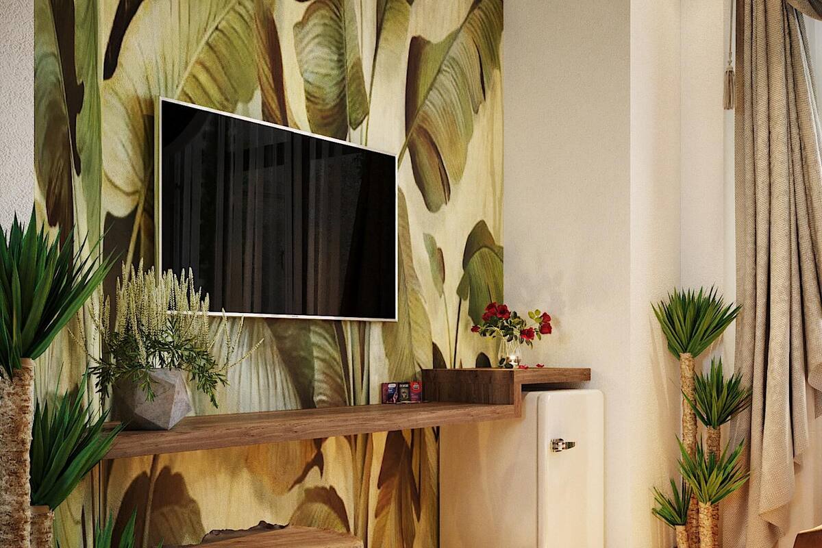 Een woonkamer met een grote flatscreen televisie aan een muur met een tropisch bladmuur, een houten salontafel, een kleine witte koelkast en verschillende potplanten.
